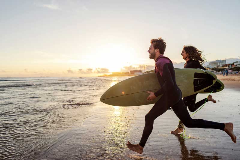 couple with surf boards running into water