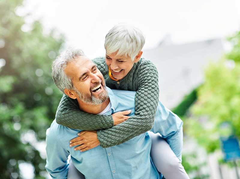 mature aged couple and man carrying woman in piggy back while they smile at each other