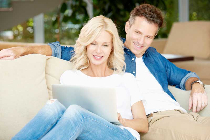 middle aged couple sitting on the couch looking at a laptop