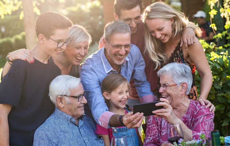 multi generation family smiling and looking at phone in garden